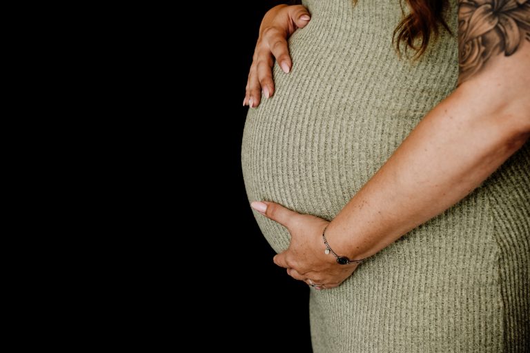Zwangerschapsshoot met zwarte achtergrond detailfoto van handen op zwangere buik