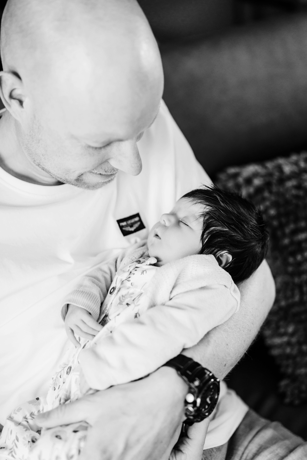 Vader houdt zijn pasgeboren baby liefdevol vast tijdens een intieme zwangerschap newbornshoot in zwart-wit stijl