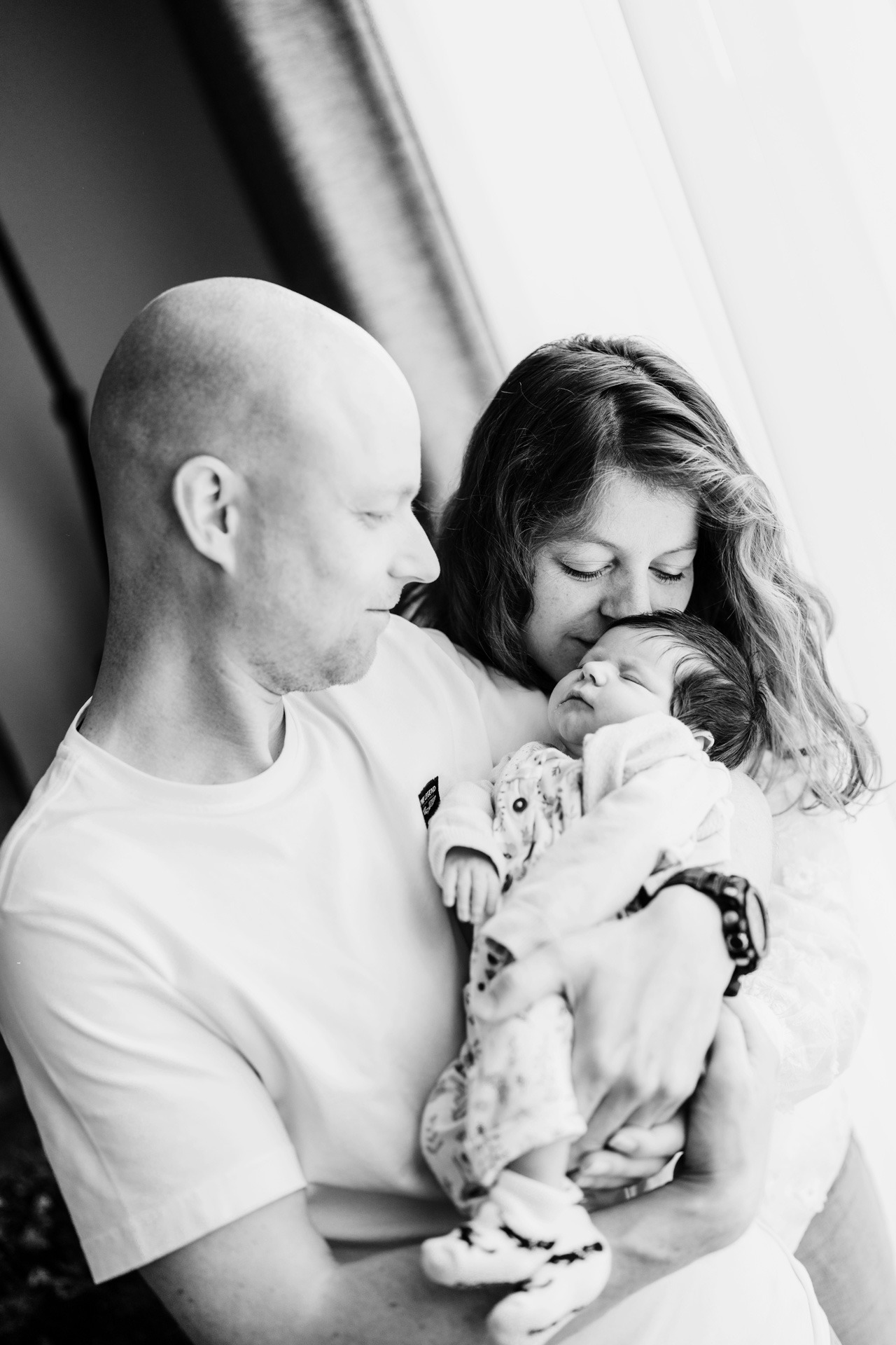 Ouders bewonderen hun pasgeboren baby samen tijdens een warme zwangerschap newbornshoot bij het raam