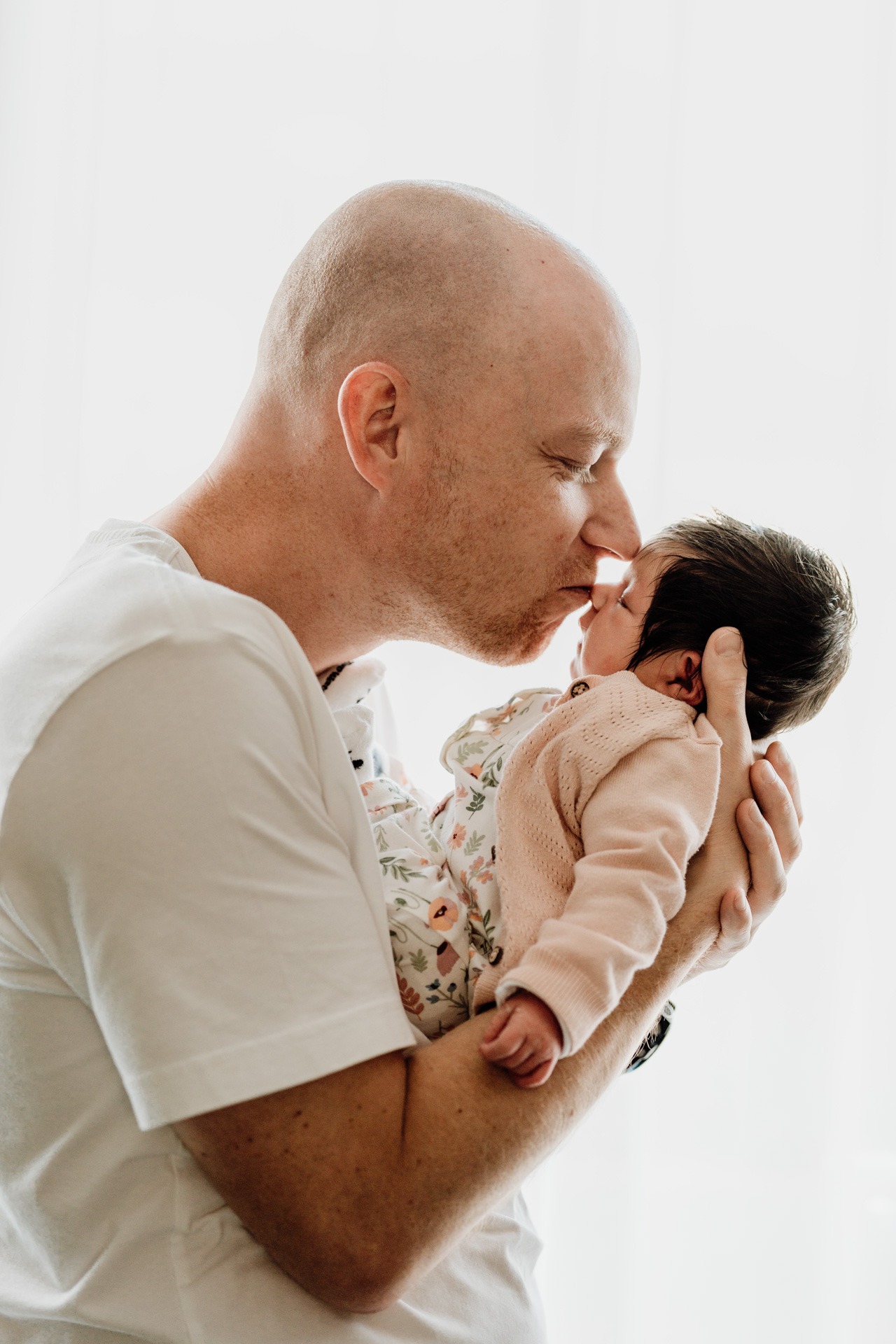 Vader geeft een zacht kusje aan zijn pasgeboren baby tijdens een liefdevolle zwangerschap newbornshoot