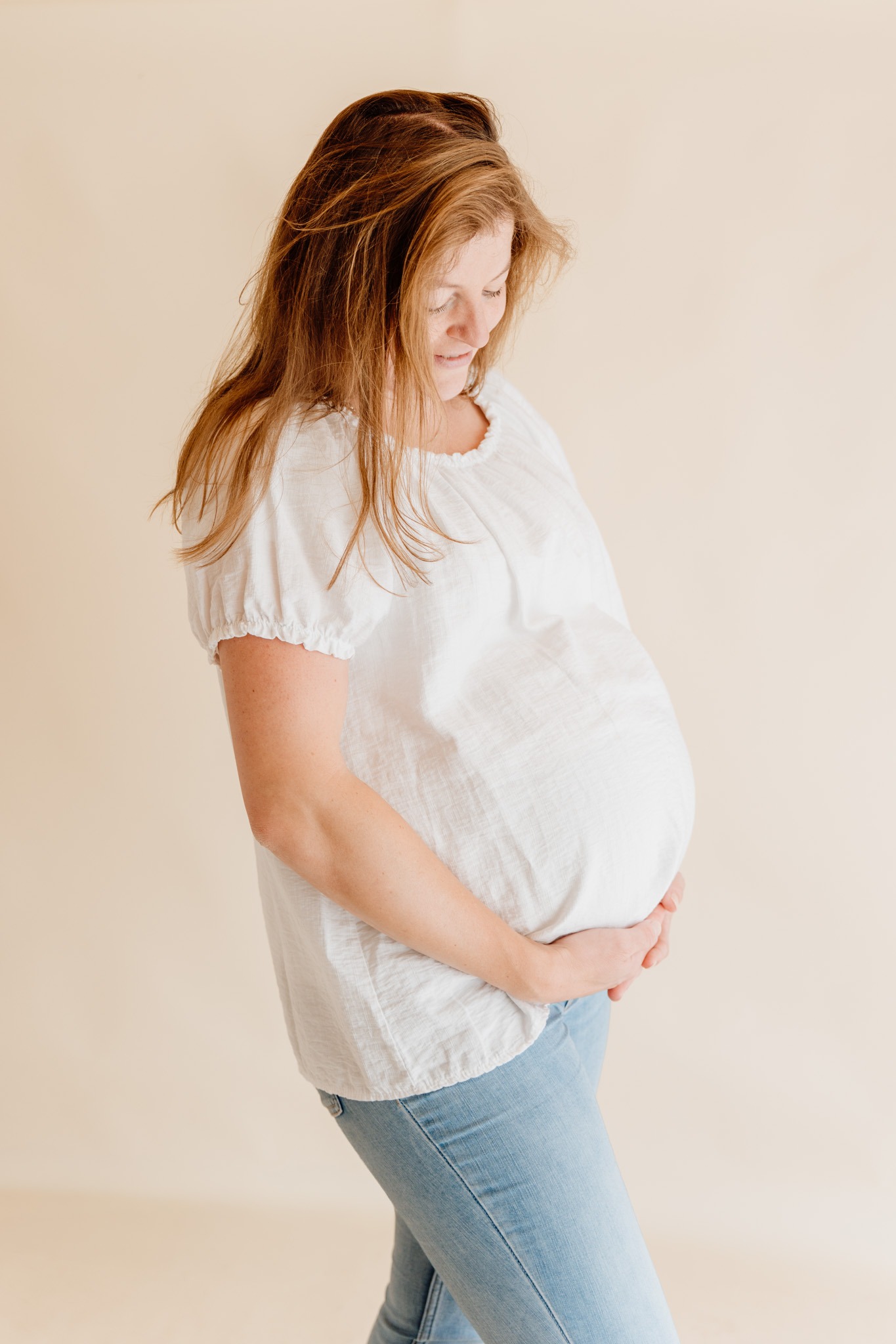 Zwangere vrouw kijkt liefdevol naar haar babybuik tijdens een rustige zwangerschap newbornshoot in de studio