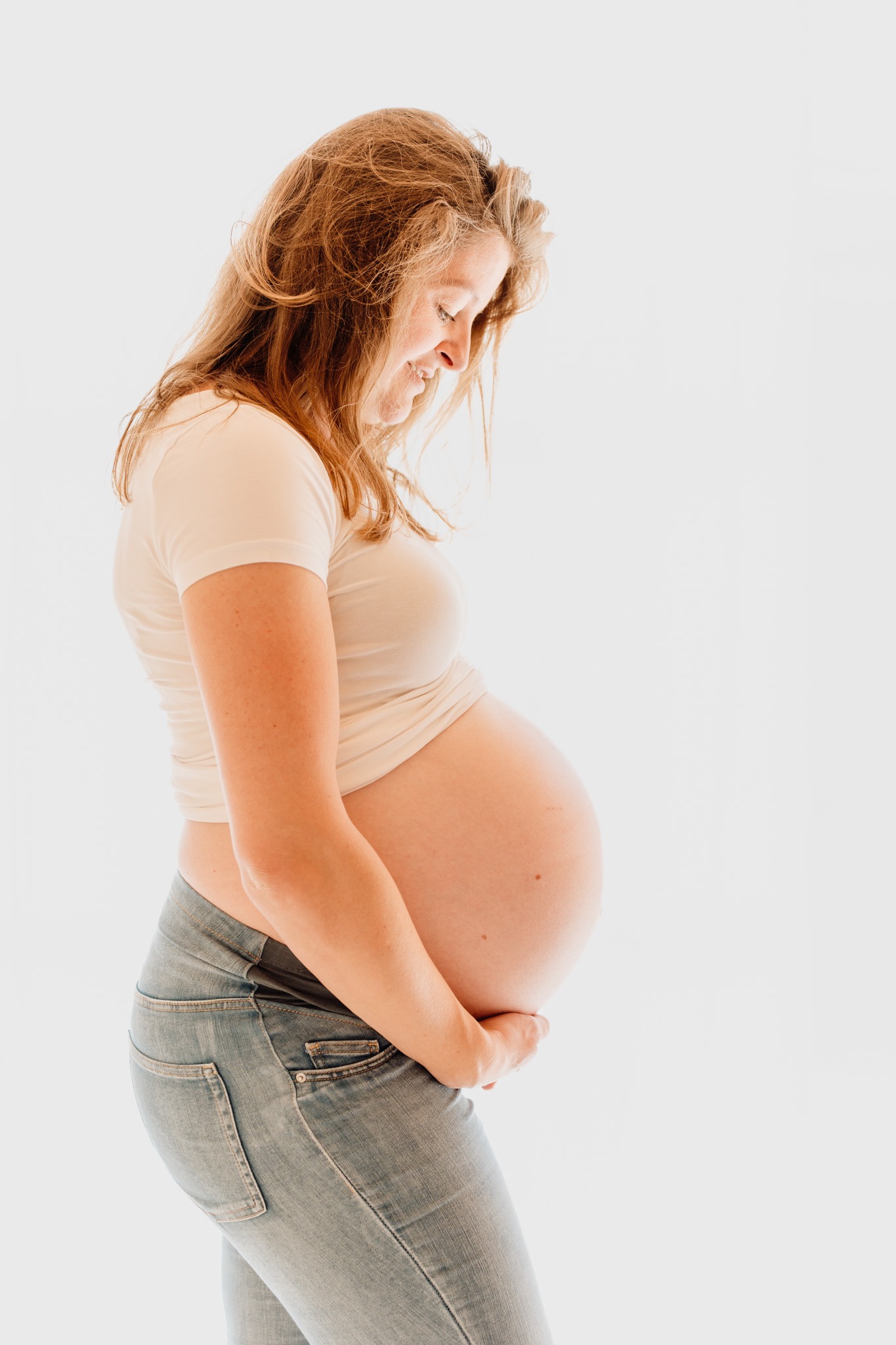 Zwangere vrouw houdt haar babybuik vast en kijkt ernaar tijdens een pure zwangerschap newbornshoot