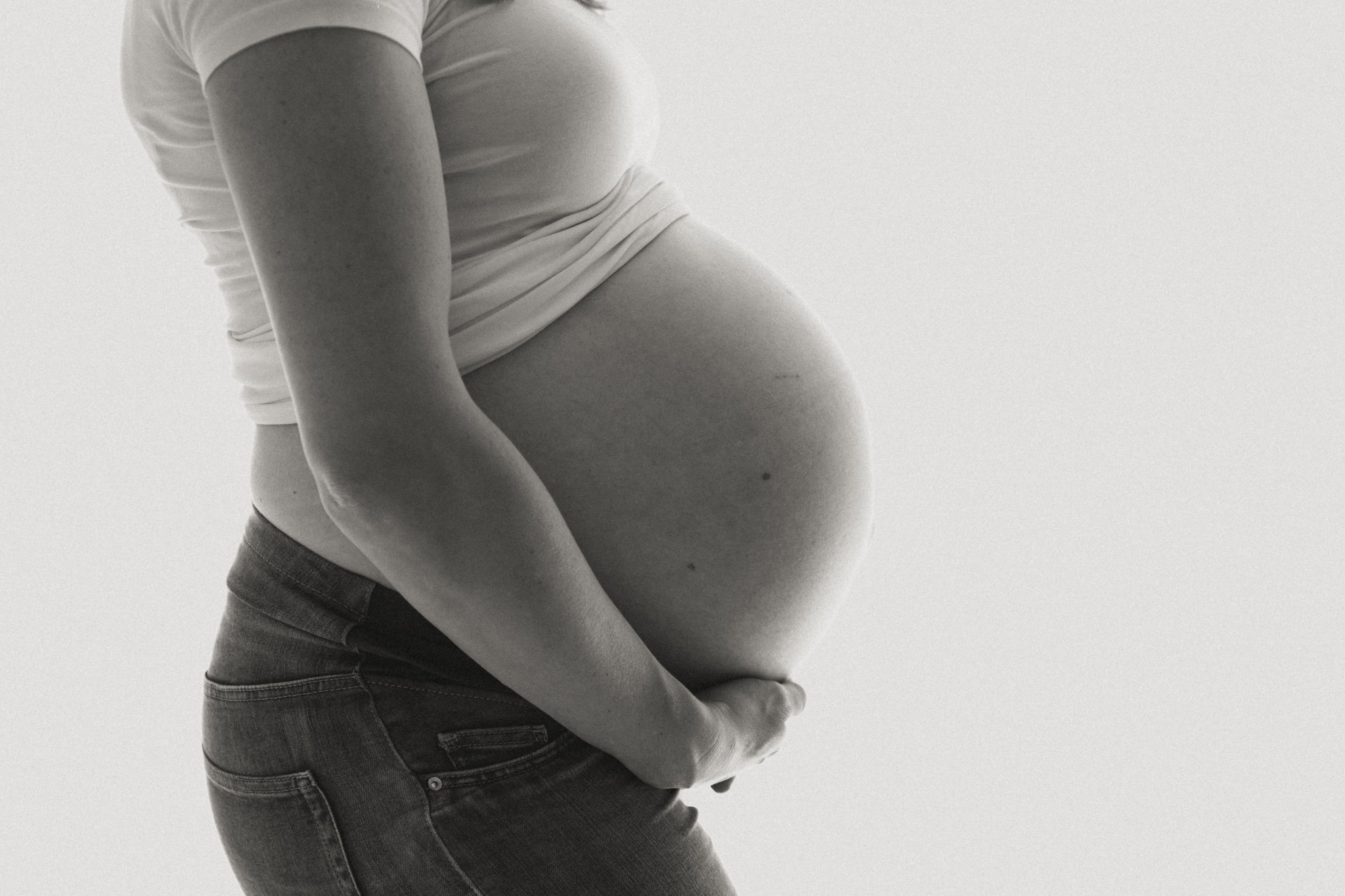 Zwart-wit detail van een zwangere buik vastgehouden door handen tijdens een zwangerschap newbornshoot