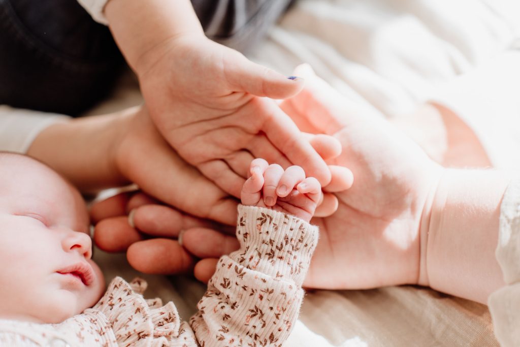 Close-up van vier handen op elkaar, papa en mama met de handjes van de grote kinderen en het kleine vuistje van newborn Yara-Nove tijdens de fotoshoot in Zuidland.