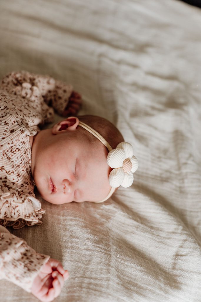 Slapende newborn Yara-Nove met een wit bloemetjeshaarbandje, liggend op een zachte linnen deken tijdens de newborn fotoshoot thuis in Zuidland.