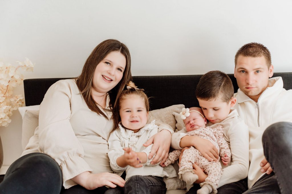 Gezin van vijf samen op de bank tijdens de newborn fotoshoot in Zuidland: papa, mama, grote broer, grote zus en pasgeboren Yara-Nove met haar bloemetjeshaarbandje.