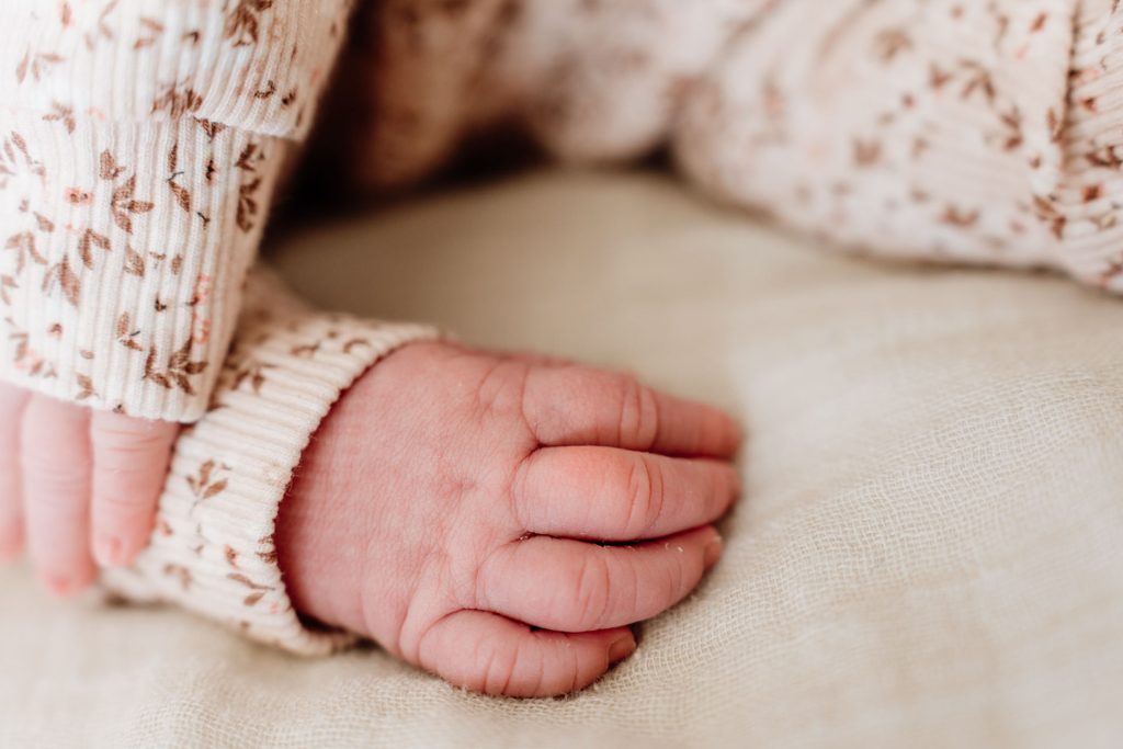 Close-up van het kleine voetje van newborn Yara-Nove dat door een grote broer of zus voorzichtig wordt vastgehouden tijdens de newborn fotoshoot in Zuidland.