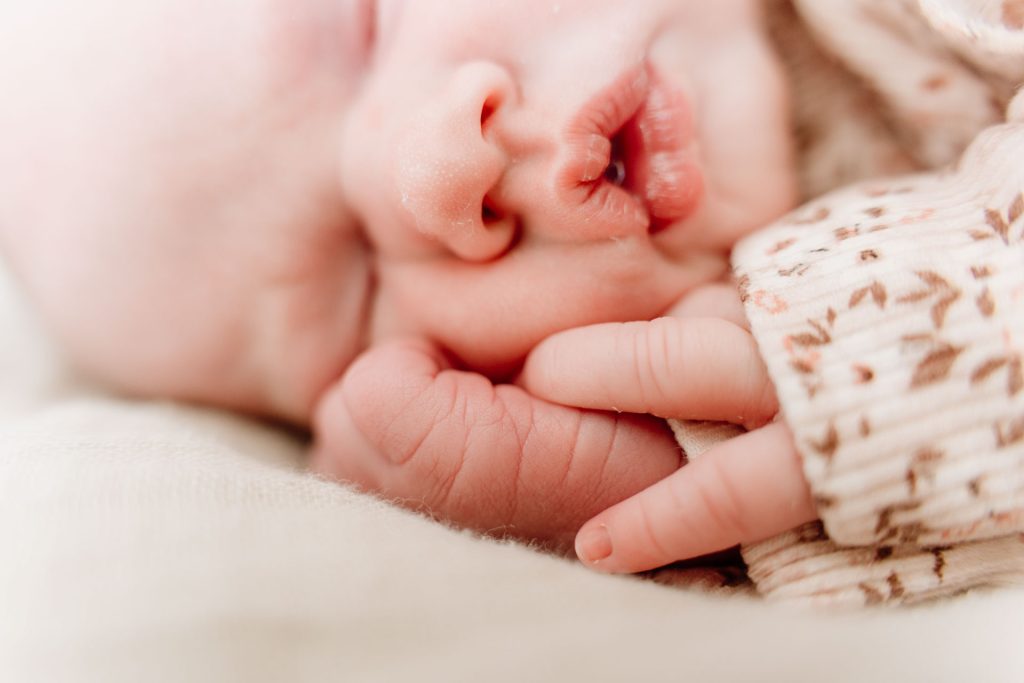 Grote broer kijkt met een brede glimlach naar slapende newborn Yara-Nove die naast hem ligt, een spontaan moment tijdens de newborn fotoshoot thuis in Zuidland.