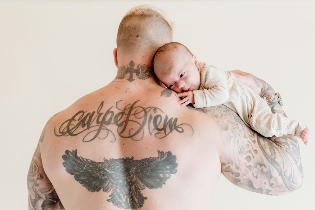 Baby Ziva liggend op de rug van Mike tijdens de newbornshoot in de studio in Zuidland, een stoer en teder beeld tegelijk
