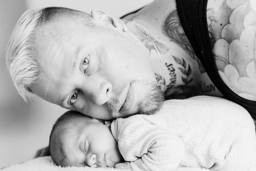Mike kijkt liefdevol naar baby Ziva tijdens de newbornshoot in de thuisstudio in Zuidland, zijn tatoeages zichtbaar op de achtergrond