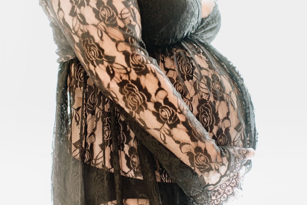 Detailfoto van de zwangere buik van Sanne omhuld door een zwarte kanten stof met rozenprint, artistieke zwangerschapsfotografie in de studio in Zuidland
