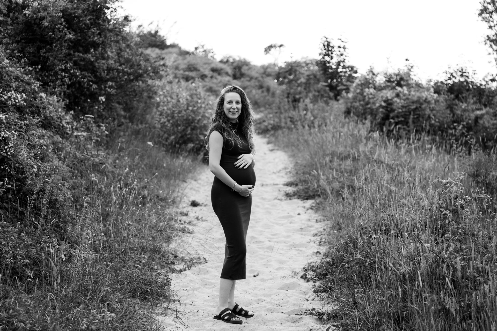 Zwangere vrouw in zwarte jurk op zandpad tijdens zwangerschapsshoot in Rockanje