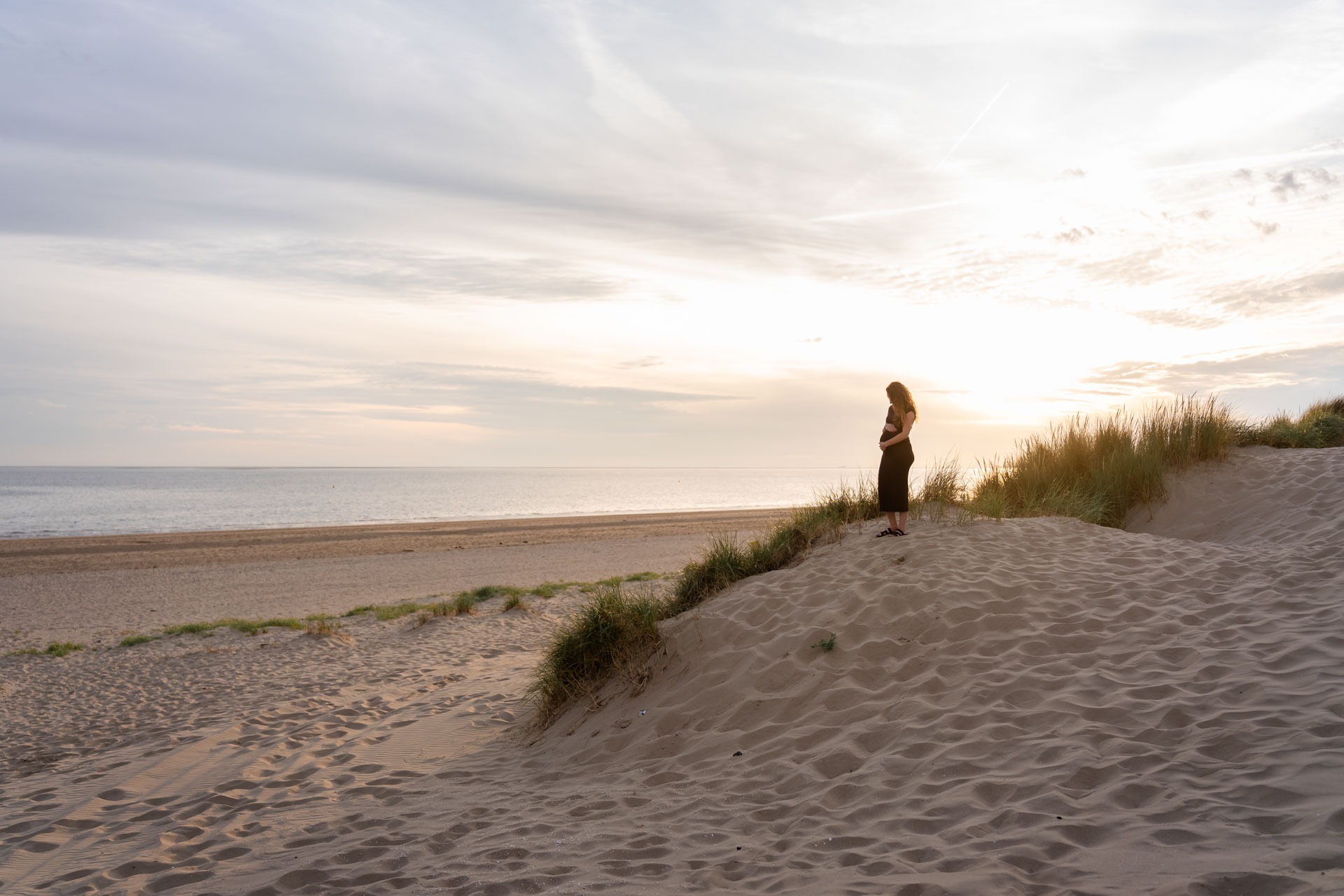 Zwangere vrouw kijkt uit over zee vanaf de duinen bij Rockanje in het avondlicht