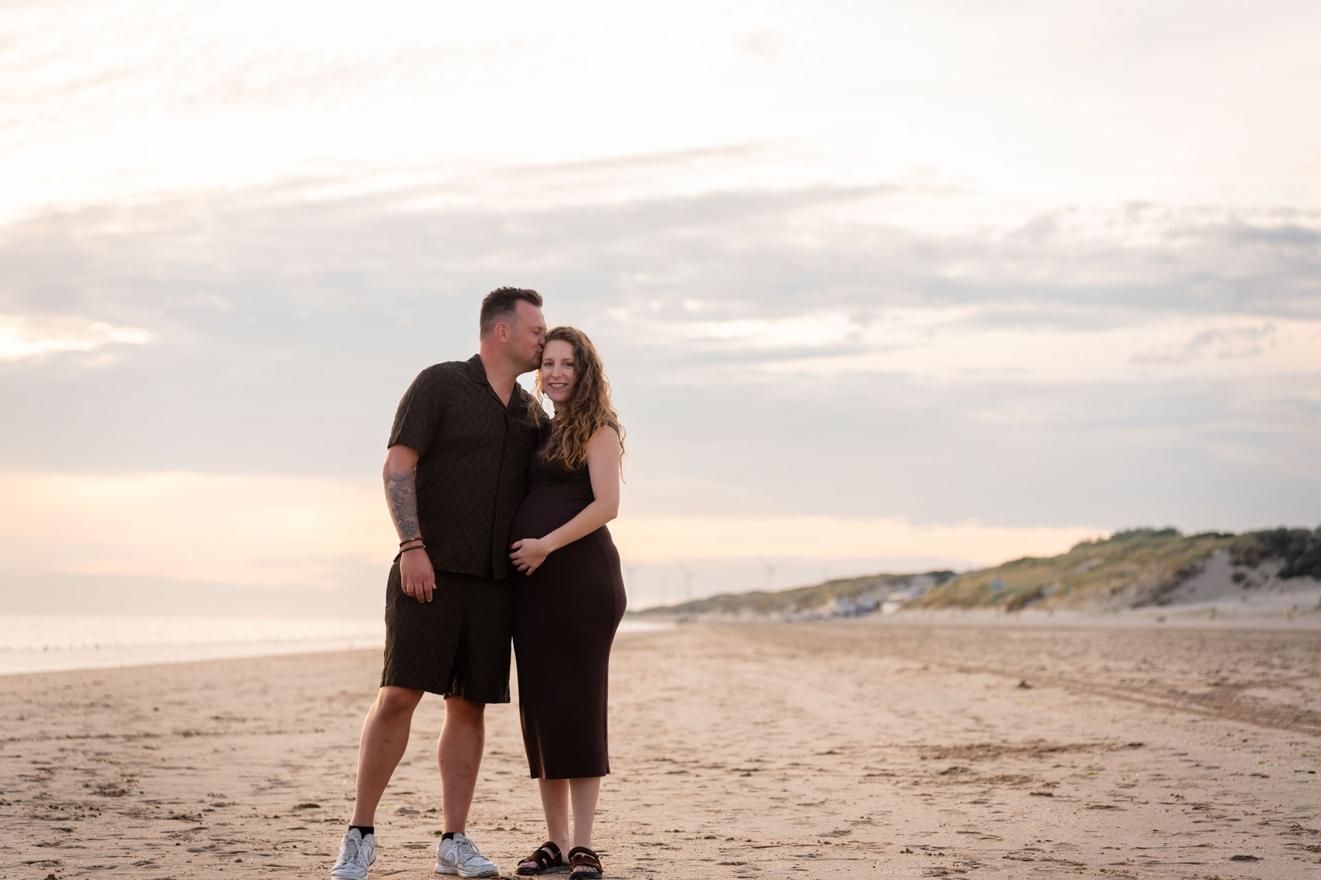 Aanstaande ouders omhelzen elkaar op het strand van Rockanje bij zonsondergang