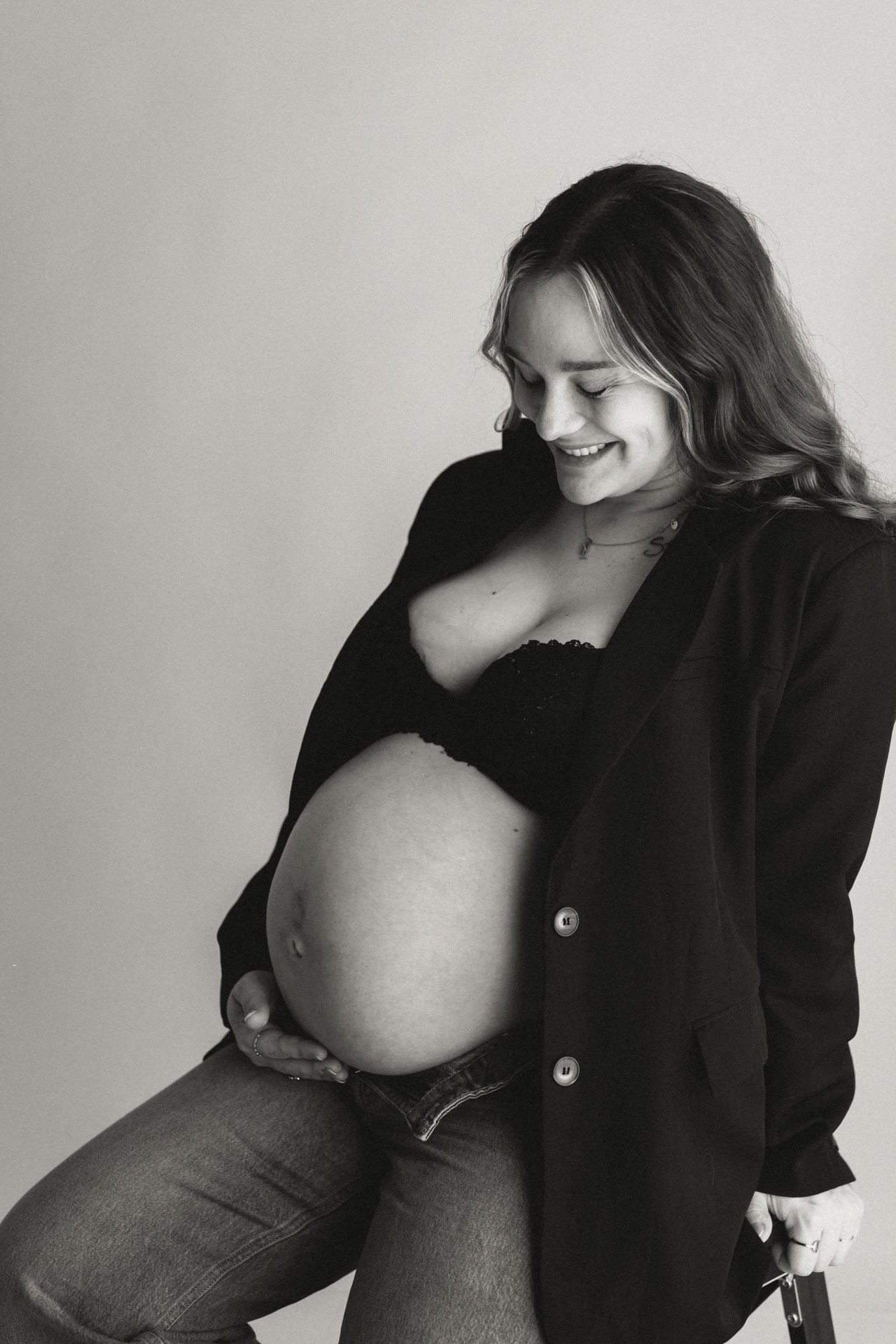 Zwart-witfoto van zwangere vrouw die lachend naar haar babybuik kijkt tijdens studioshoot bij Daphne's Fotografie