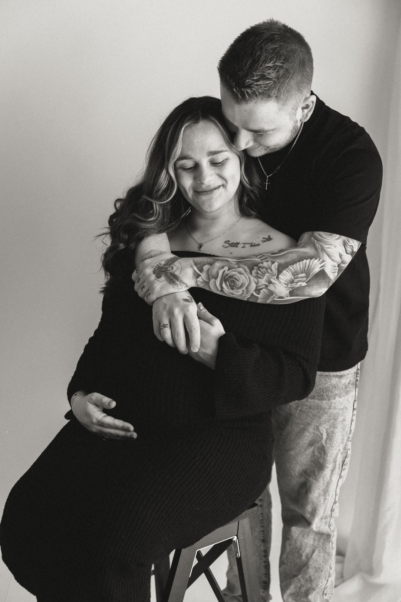Zwart-witfoto van partner die zwangere vrouw van achteren omhelst tijdens studioshoot in Zuidland