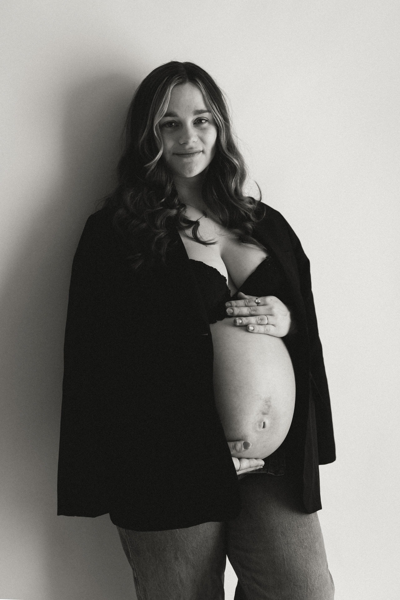 Zwart-wit portret van zwangere vrouw met blote babybuik in zwarte blazer, studio zwangerschapsshoot Zuidland