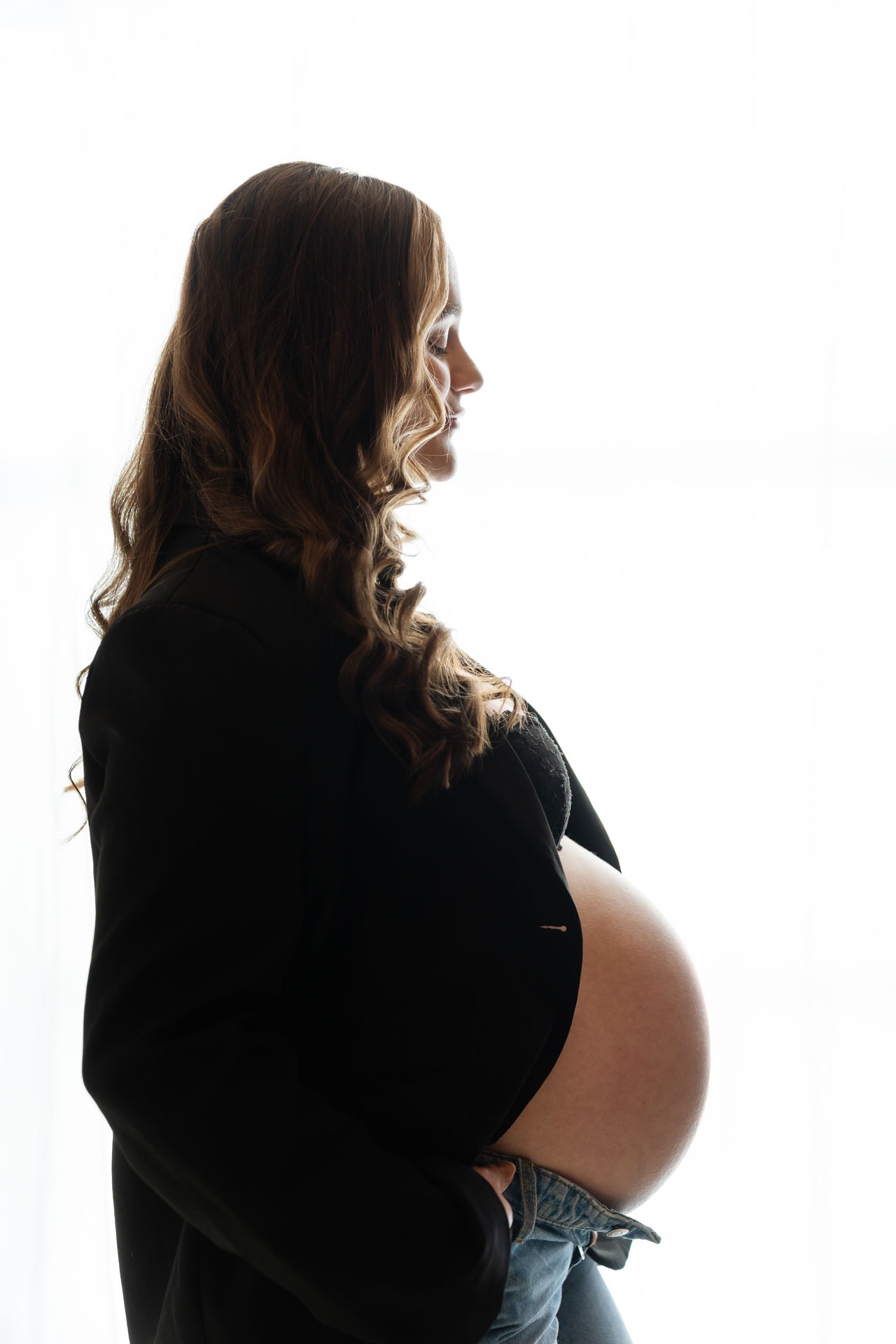 Silhouet van zwangere vrouw met babybuik voor lichte achtergrond tijdens zwangerschapsshoot in de studio in Zuidland