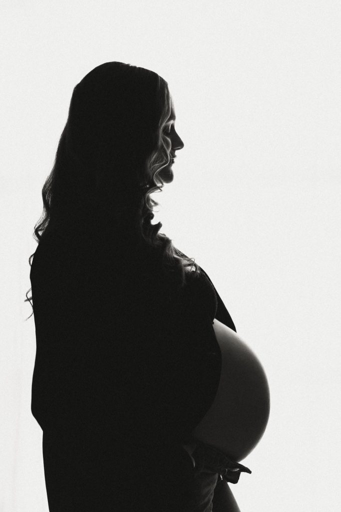 Zwart-wit silhouet van zwangere vrouw met ronde babybuik tegen licht doek, zwangerschapsshoot studio Zuidland