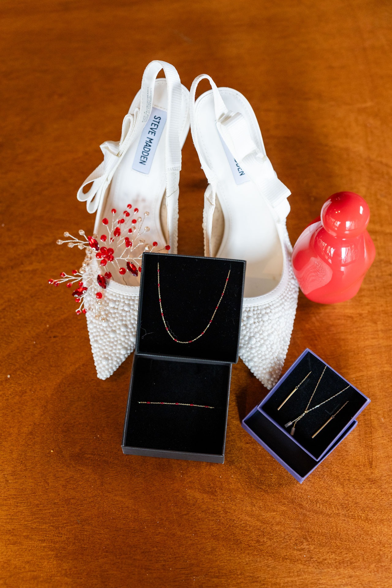Parelmoeren bruidsschoenen met sieraden en rood parfum, detailfoto door trouwfotograaf Hellevoetsluis