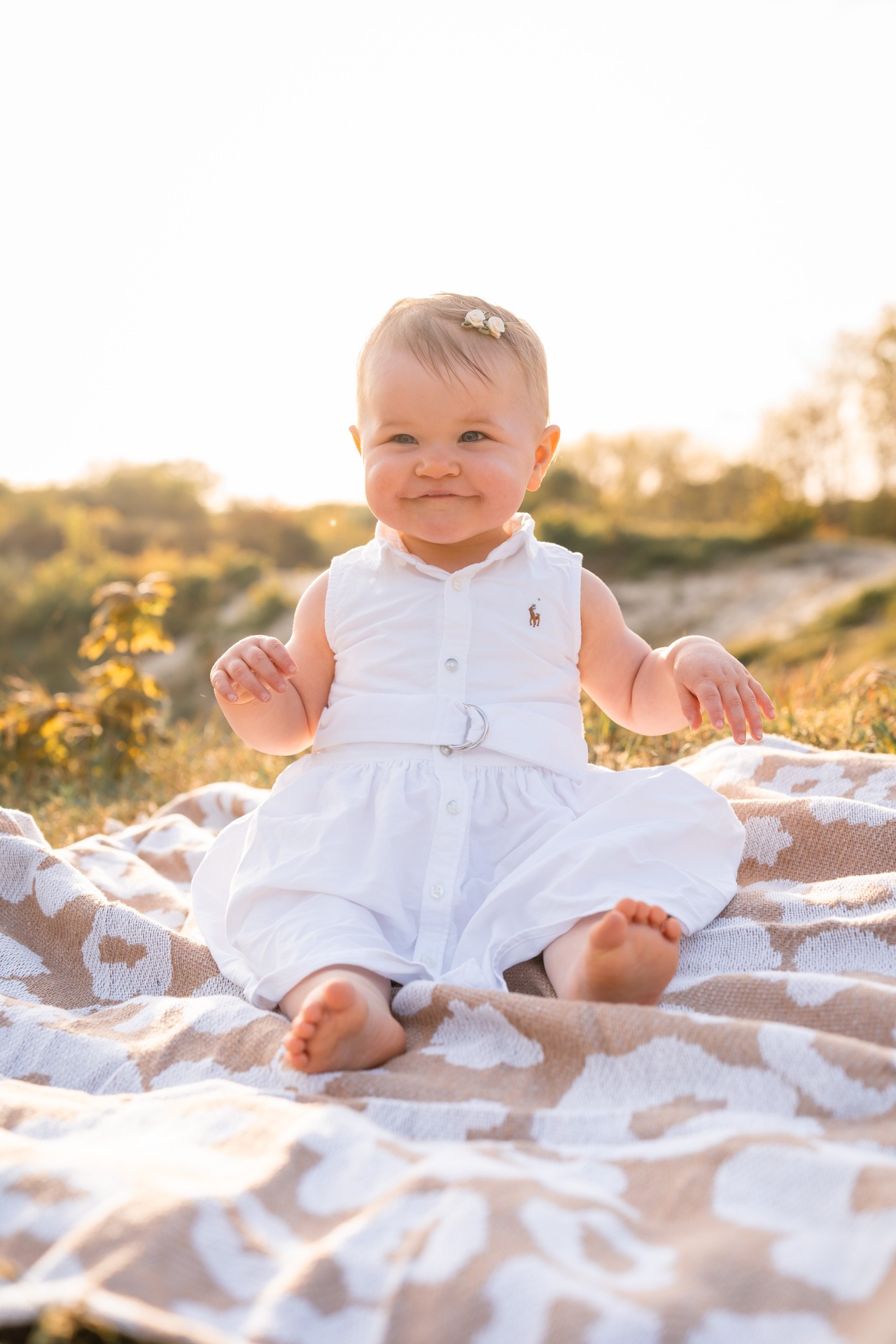 Meisje van één in witte jurk zit in het zand tijdens familieshoot strand Rockanje in het gouden avondlicht