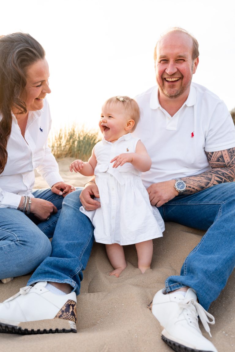 Lachend meisje van één tussen haar ouders in het zand bij familieshoot strand Rockanje