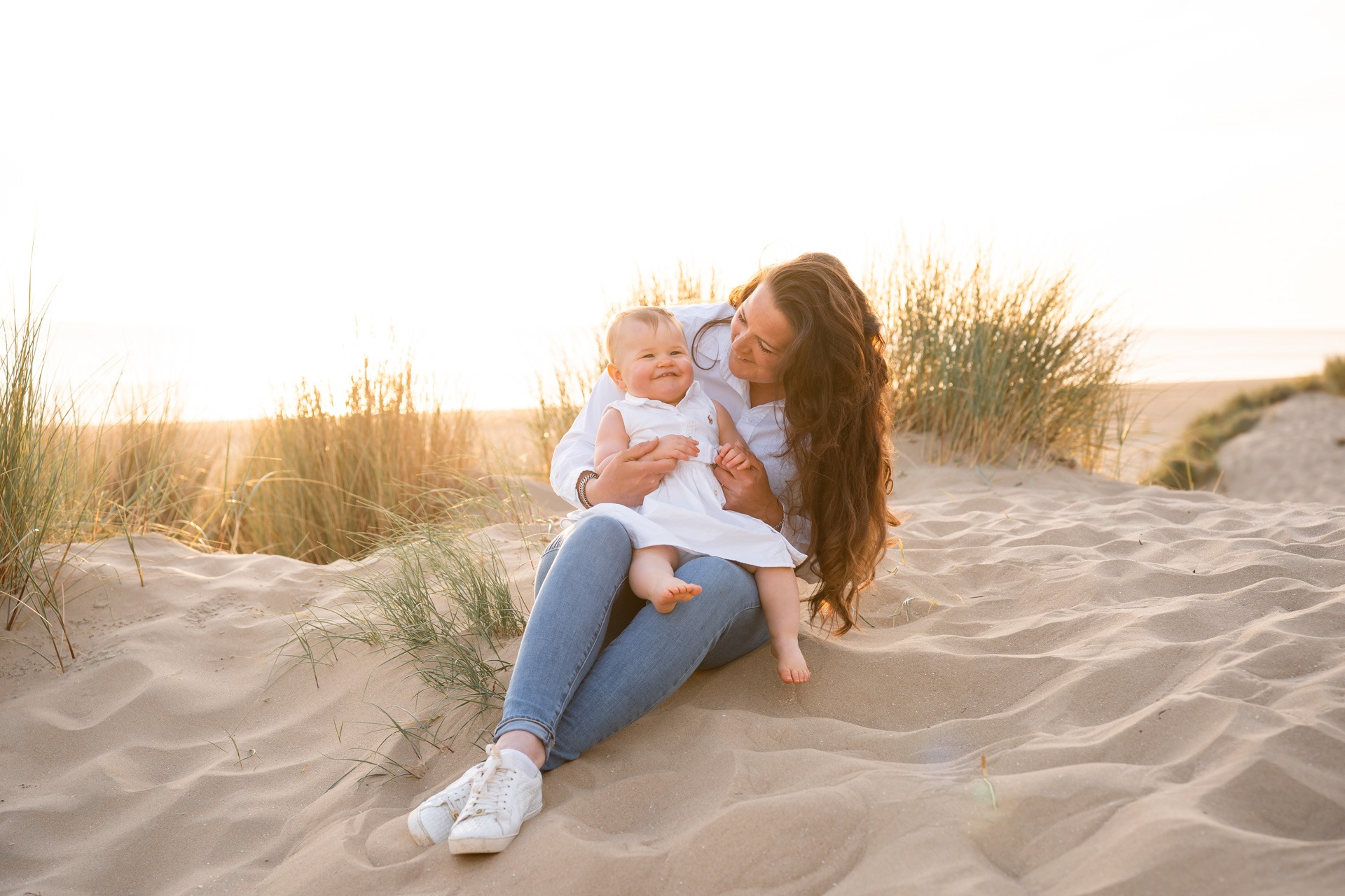 Moeder houdt haar dochtertje op schoot in de duinen bij zonsondergang op het strand van Rockanje
