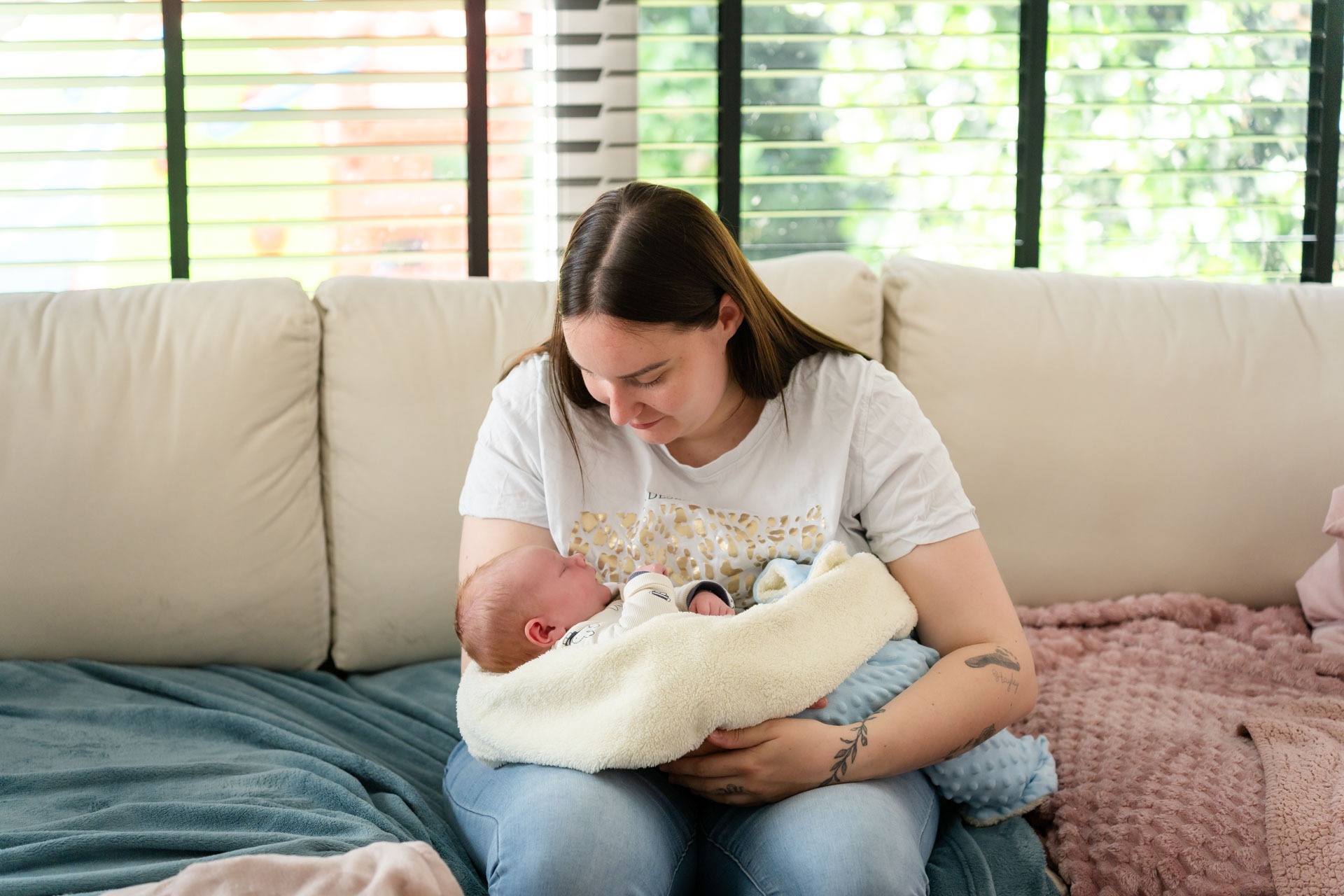 Mama houdt haar pasgeboren baby vast op de bank tijdens newbornshoot aan huis