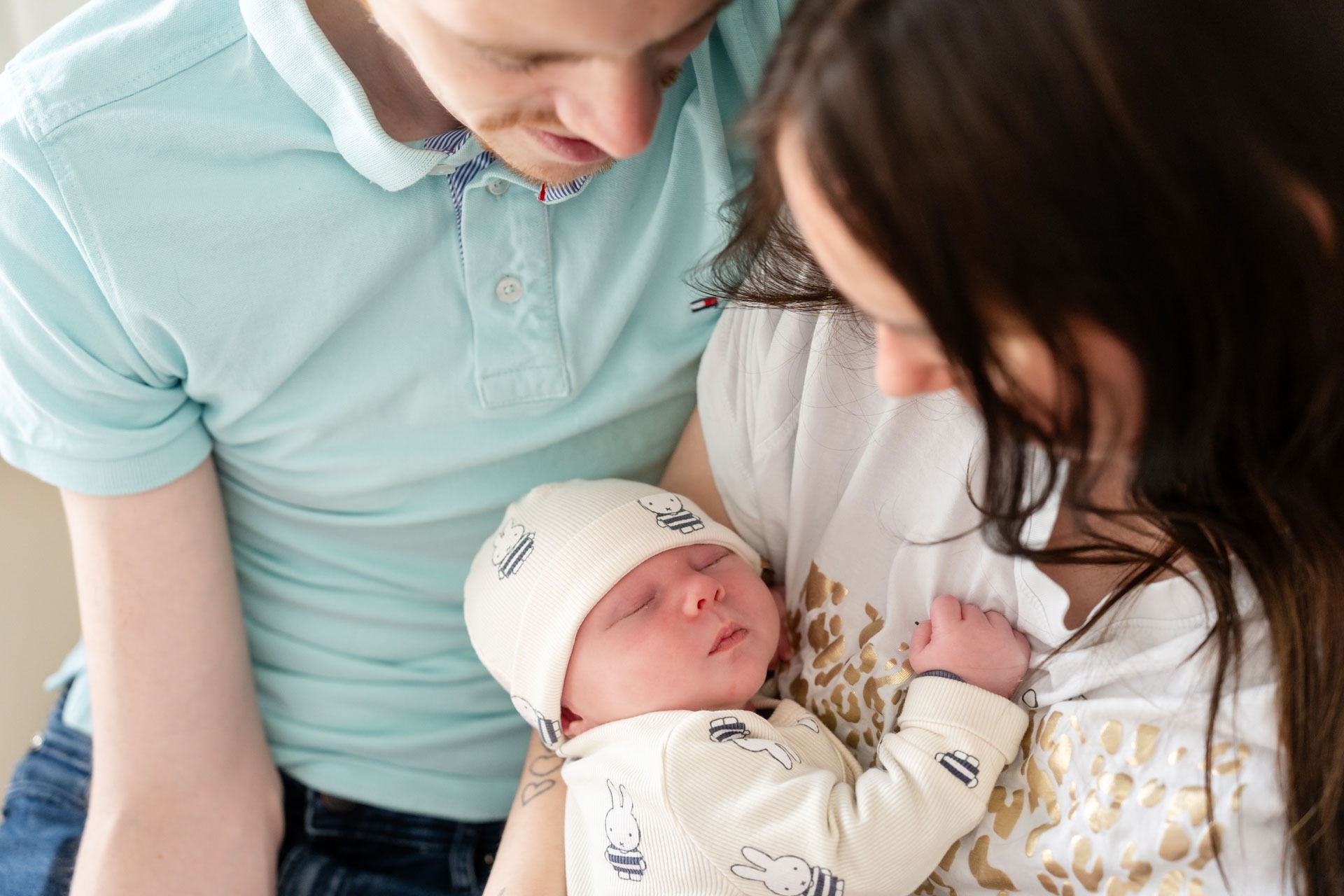 Papa en mama kijken naar hun slapende pasgeboren baby tijdens newbornshoot aan huis Zwartewaal