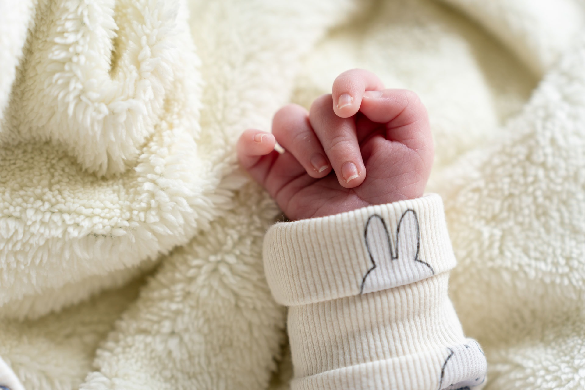 Klein knuistje van pasgeboren baby op zacht dekentje tijdens newbornshoot aan huis
