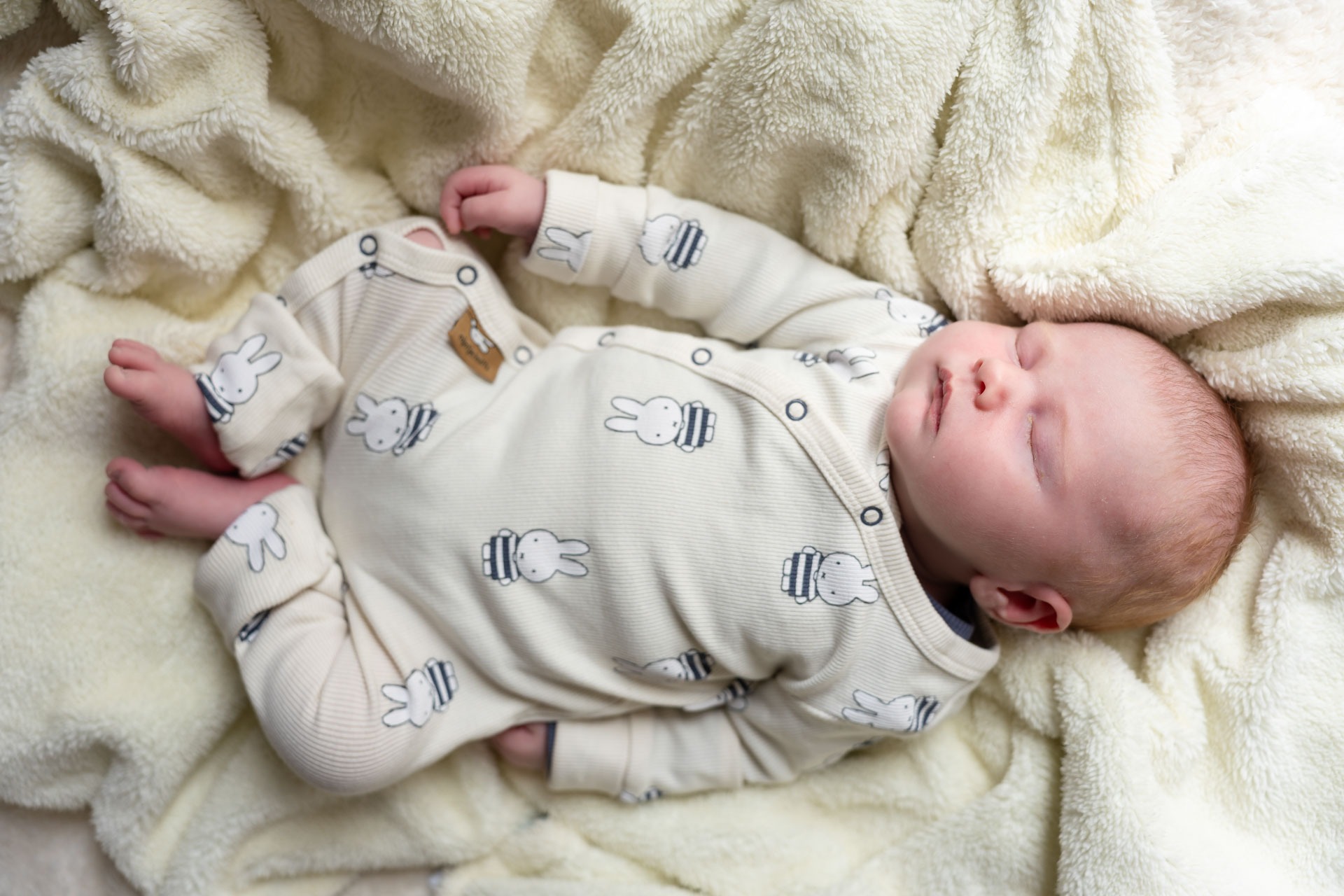 Pasgeboren baby in nijntje-pakje op crème dekentje tijdens newbornshoot aan huis Zwartewaal