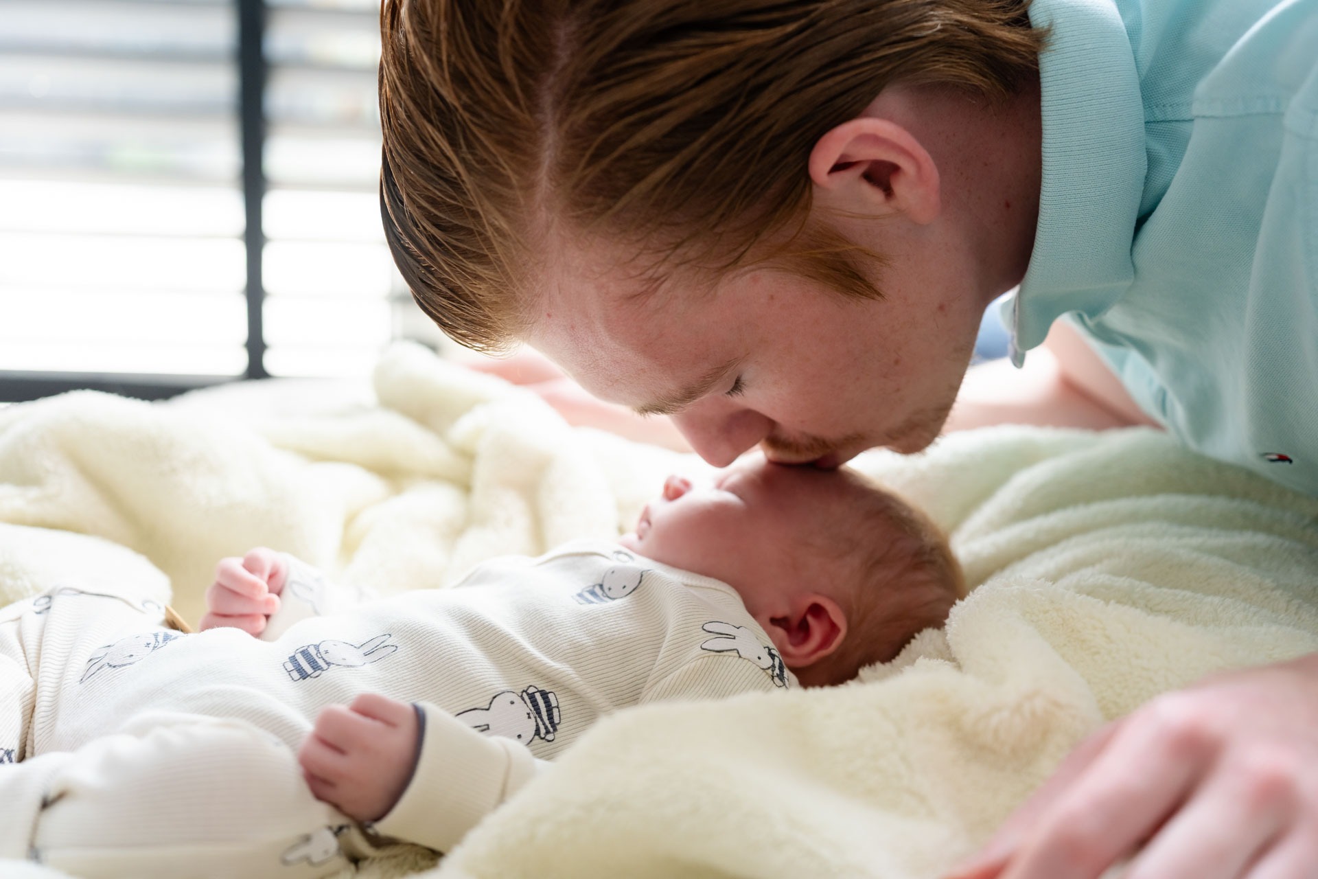 Papa geeft kusje op het hoofdje van zijn pasgeboren zoontje tijdens newbornshoot aan huis Zwartewaal