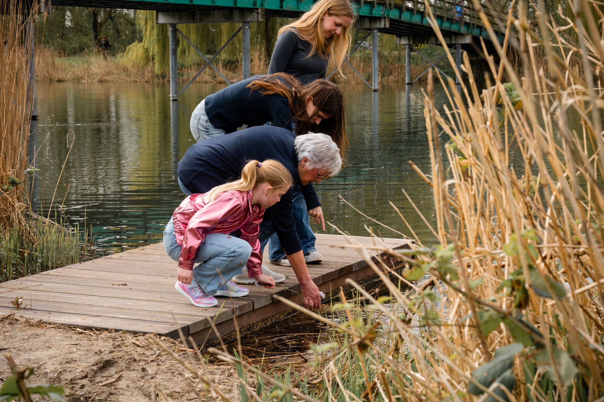 Familie bukt samen bij de vijver om iets in het water te bekijken tijdens familieshoot in Abbenbroek