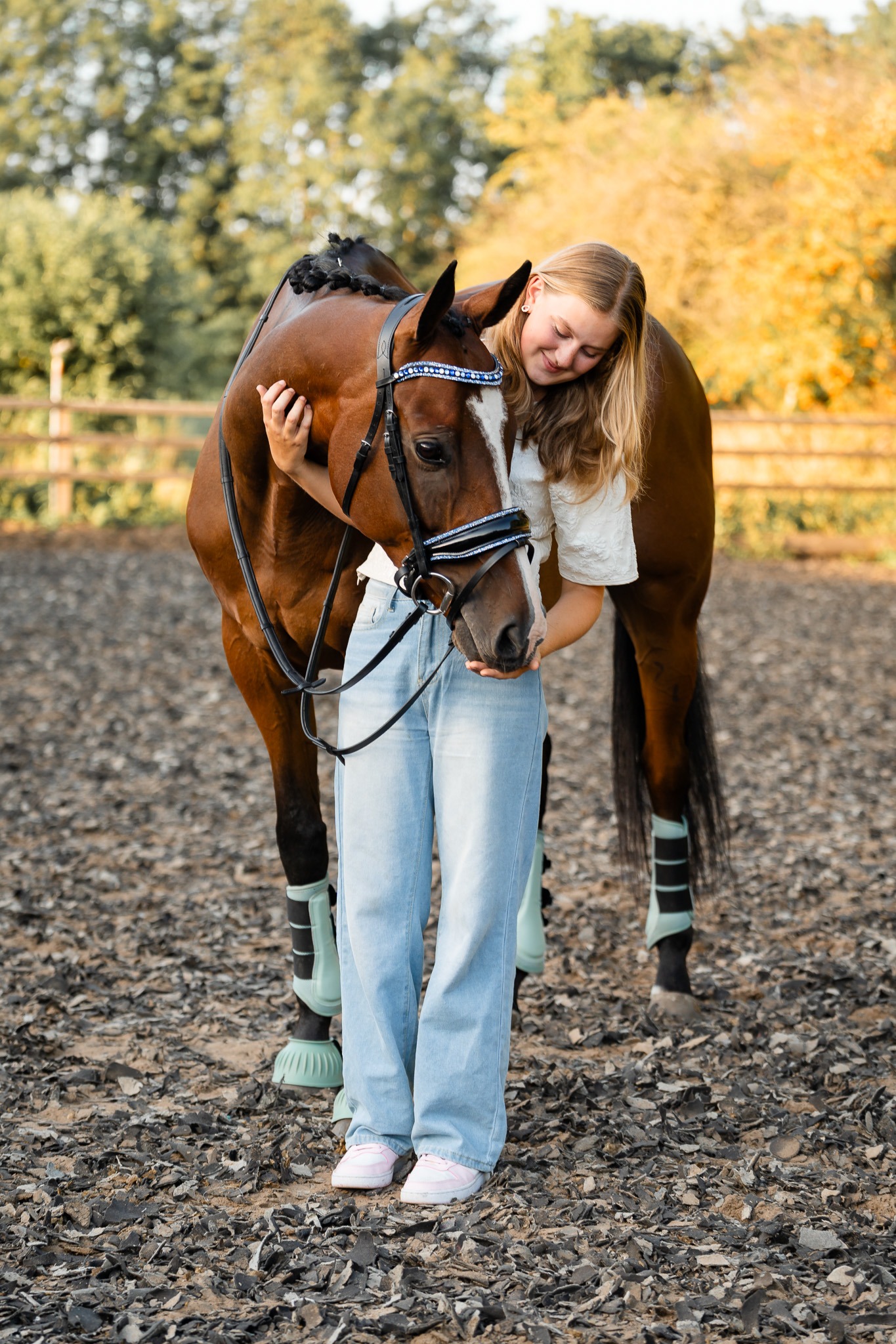Meisje in spijkerbroek knuffelt haar bruine paard op de werf van Horse World Tinte