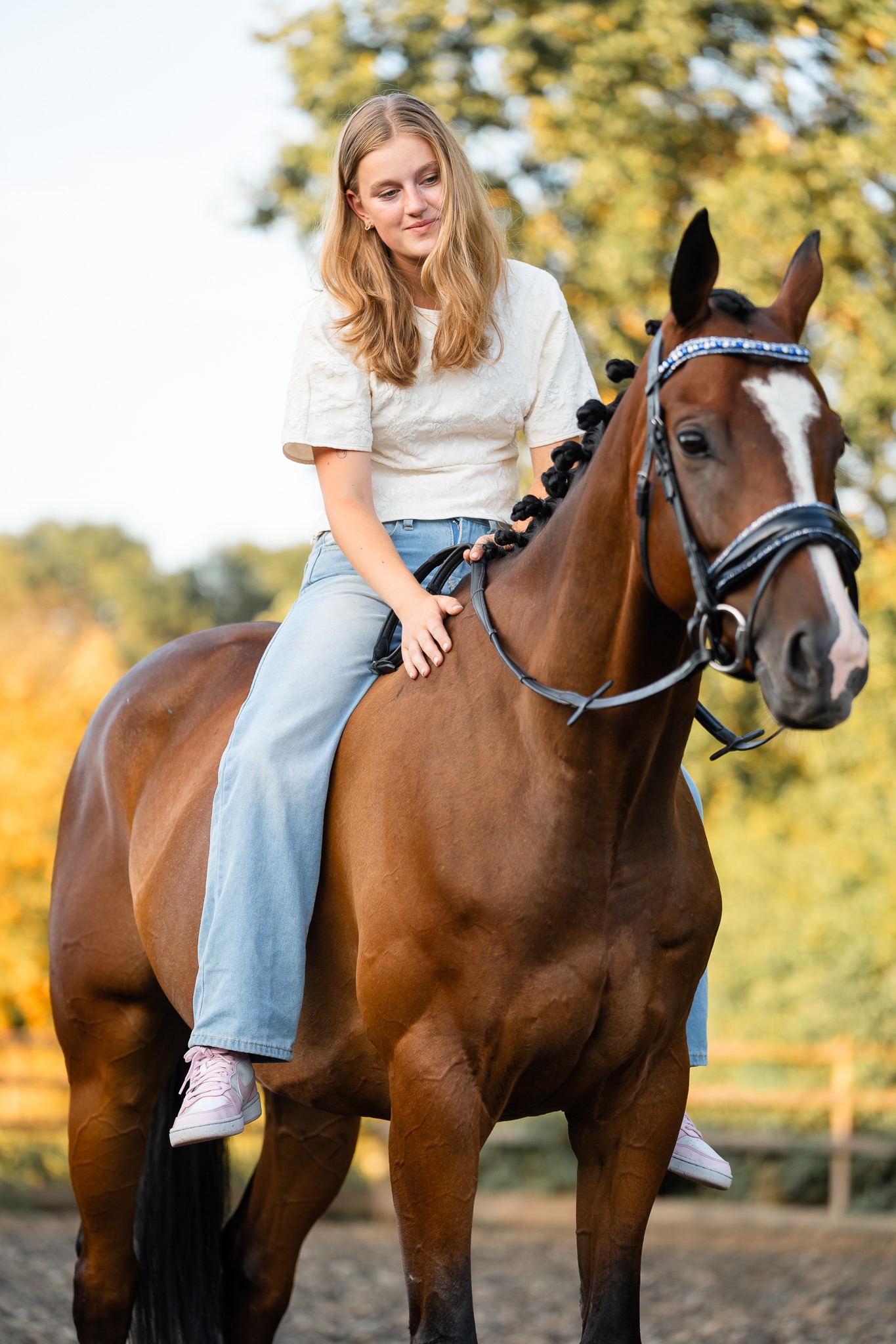 Meisje zit op haar bruine paard en kijkt lachend in de camera
