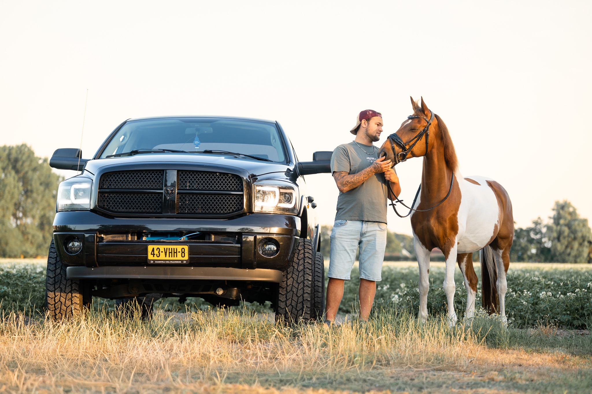 Broer bij zijn zwarte pick-up met zus en bonte pony in het veld